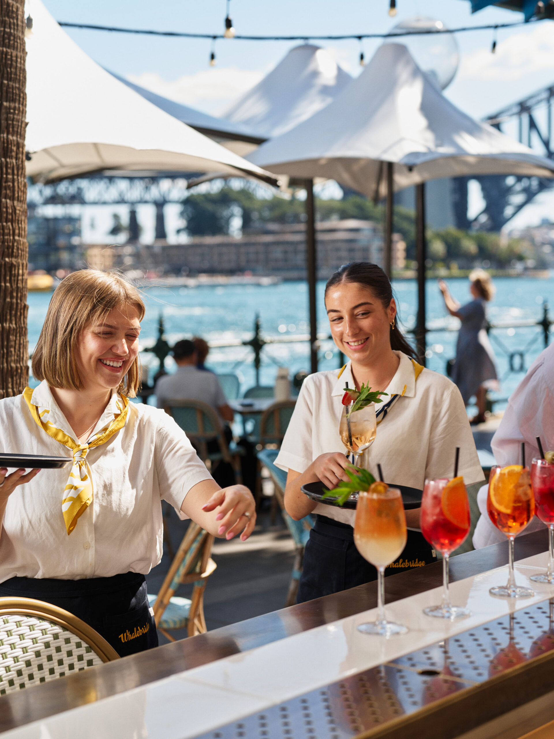 Staff serving spritzes at the Whalebridge bar, with the Sydney Harbour Bridge behind